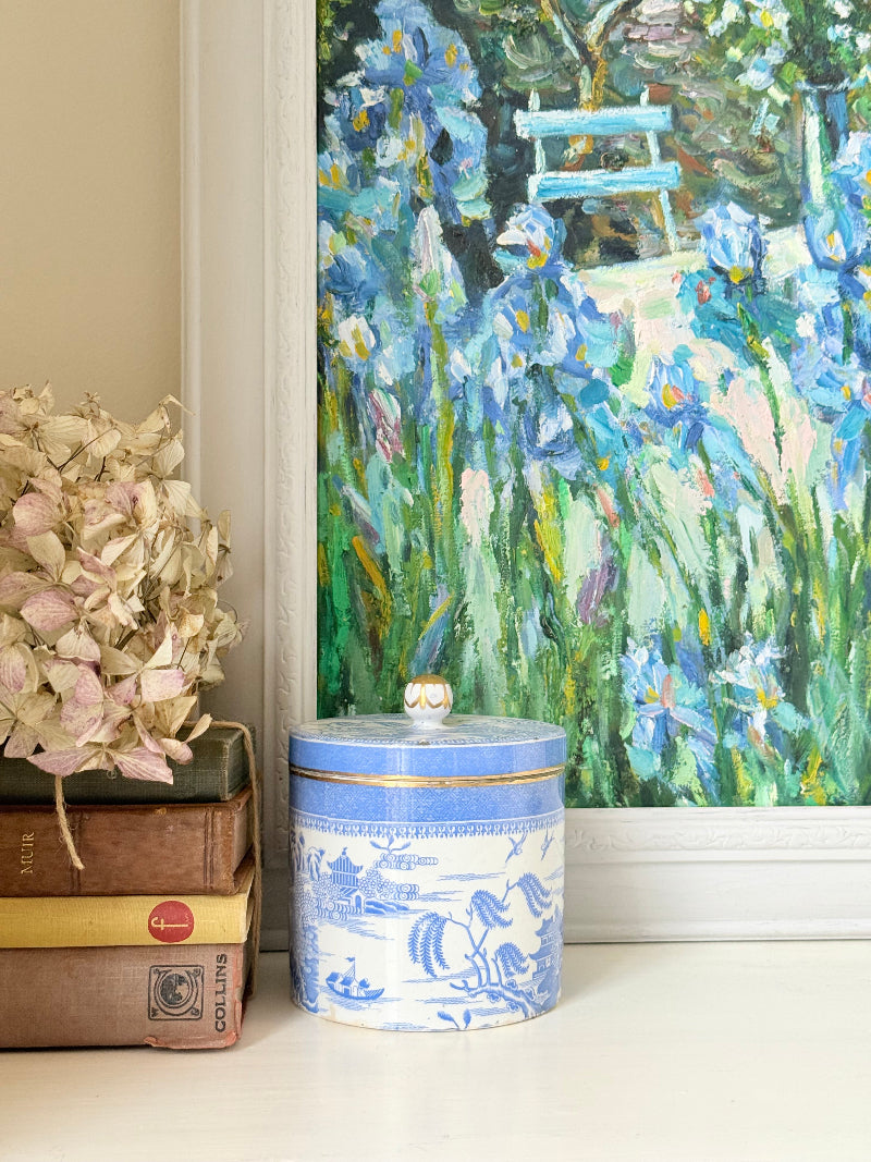 Framed impressionist-style oil painting of blue irises and garden scene, photographed on a white surface
