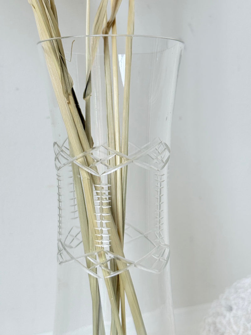 Vintage clear glass cylinder vase with etched leaf design, photographed on a white surface.