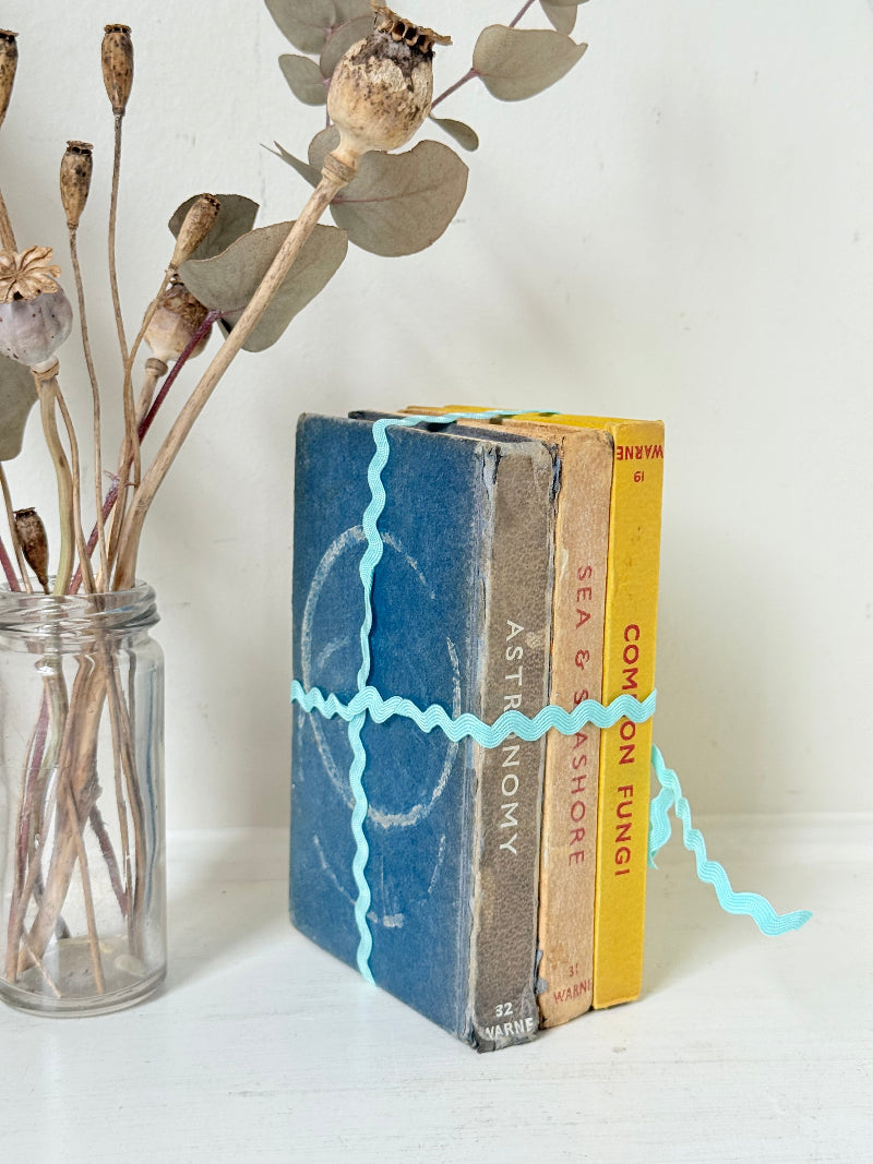 Vintage small decorative book bundle in yellow, brown and grey with turquoise ribbon, photographed on a white surface