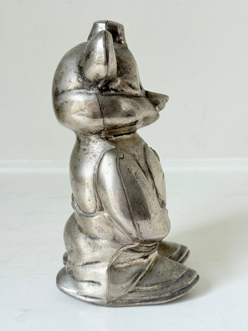 Vintage silver tone metal bear money box with coin slot on top, photographed on a white surface.