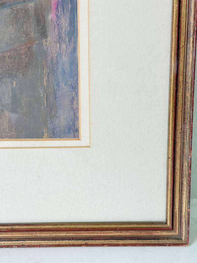 Close-up of the corner of a framed artwork, showing a distressed multi-layered wooden frame with gold leaf and reddish-brown tones, a cream mat, and a blue-gray abstract painting.