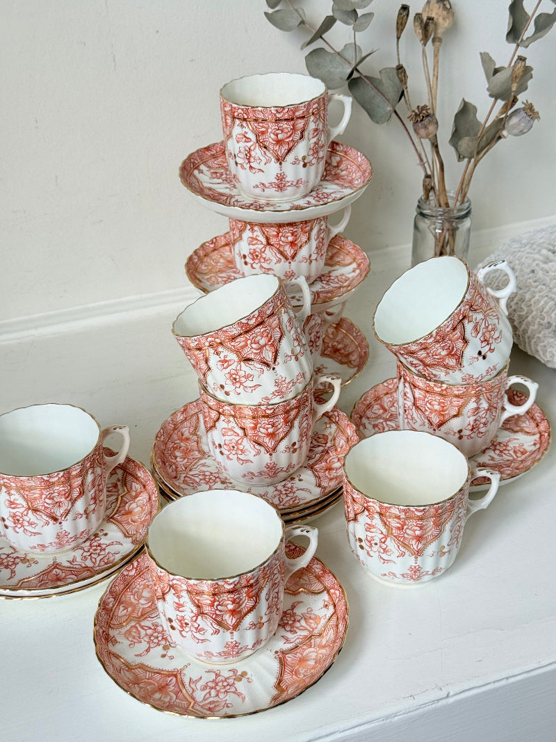 Vintage coral transferware coffee cans and saucers with scalloped edges and gold accents, set of ten, styled on a white surface.