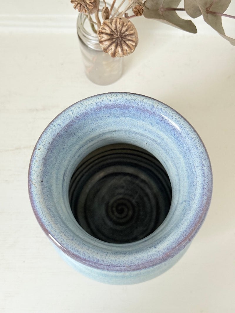 Studio pottery vase with sky blue glaze, indigo rim, and natural red clay base, photographed on a white surface