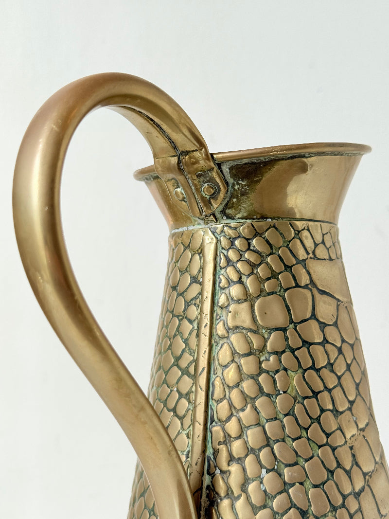 Vintage brass jug with alligator patterned surface, photographed against a white background.