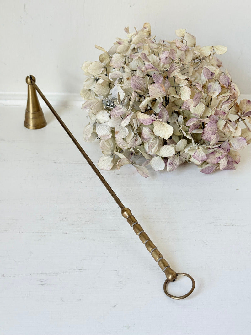 vintage brass candle snuffer with twisted handle and cone-shaped head photographed on white surface