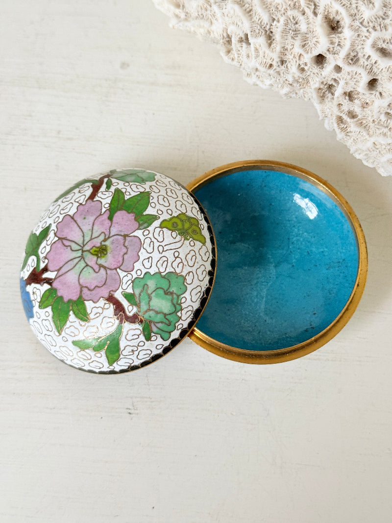 Vintage brass and enamel cloisonne trinket box with floral lid and turquoise interior photographed on a white surface