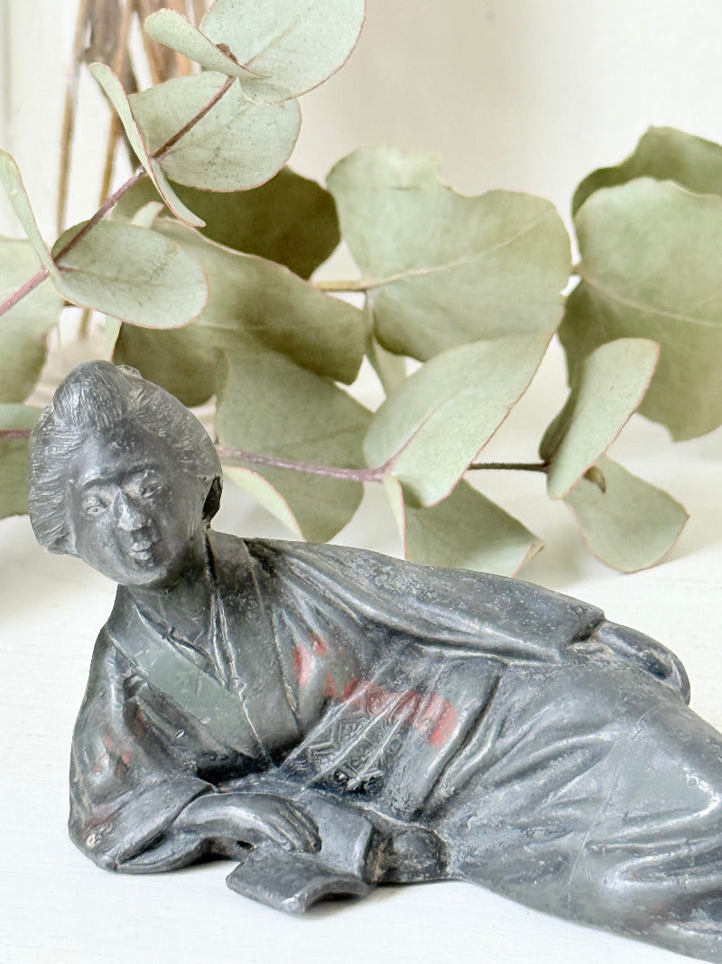 antique japanese bronze reclining lady with impressed marks to base photographed on white surface with foliage background