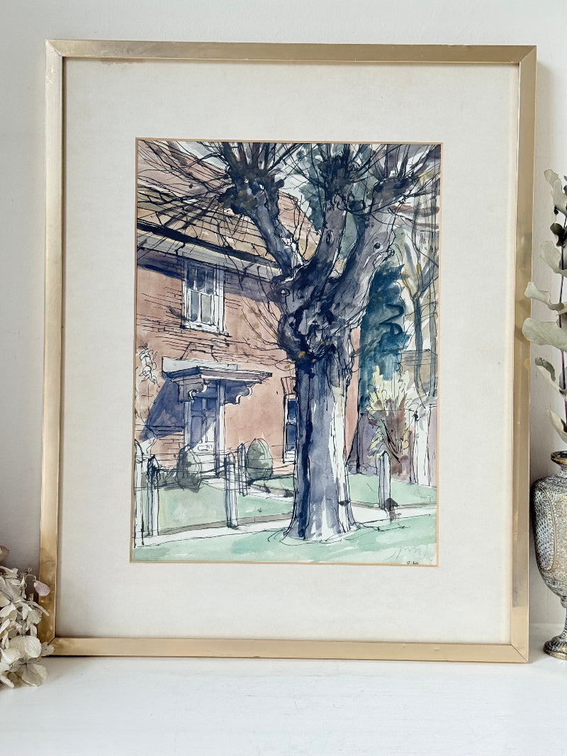 Framed vintage watercolour painting of a large tree and brick house, photographed on a white surface.