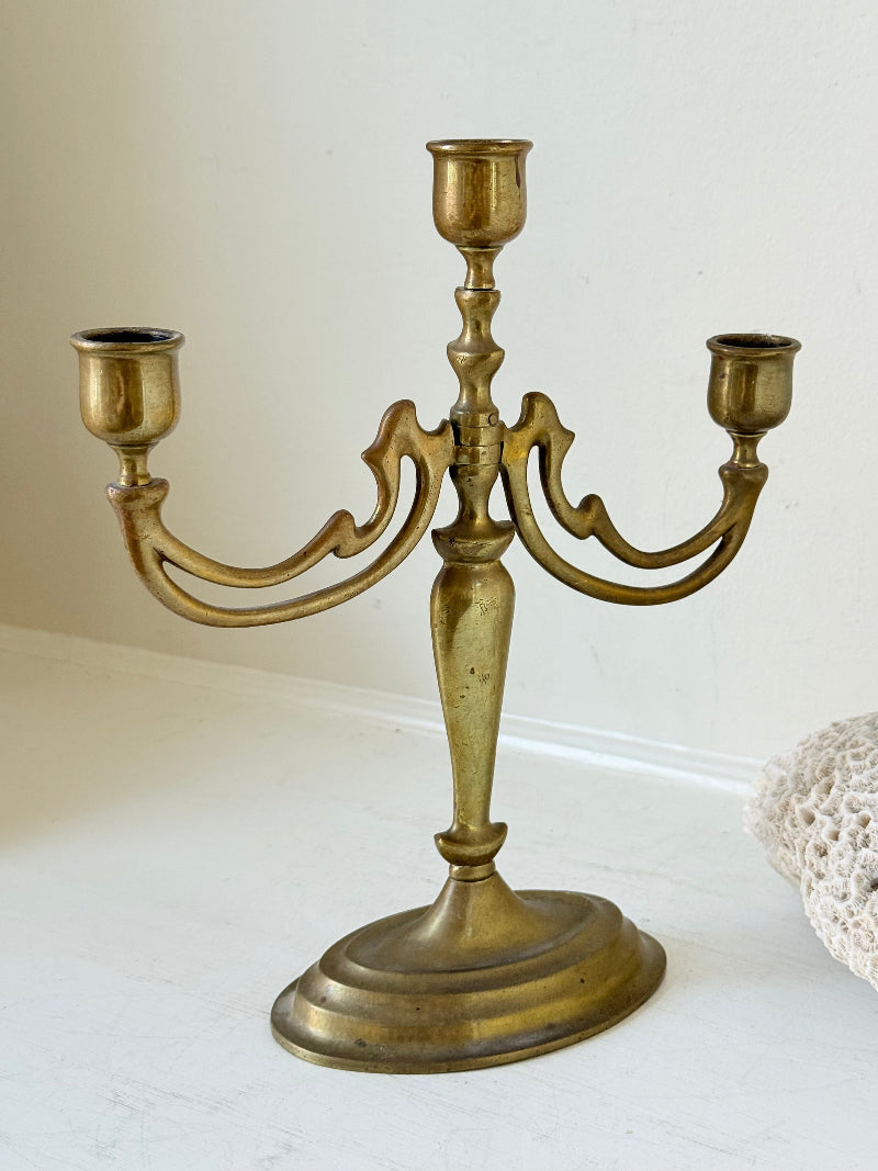 Vintage brass three-arm candelabra with curved arms and soft patina, photographed on a white surface