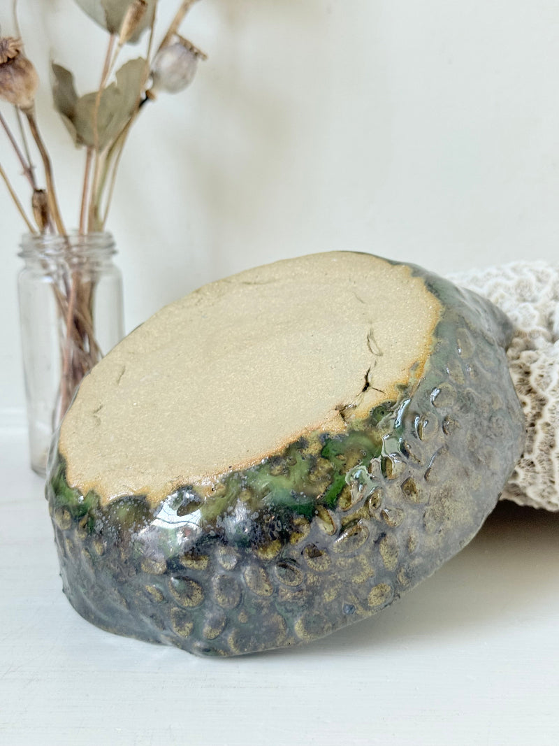 Studio pottery olive bowl with green and charcoal glaze, photographed on a white surface