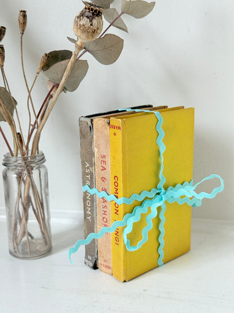 Vintage small decorative book bundle in yellow, brown and grey with turquoise ribbon, photographed on a white surface