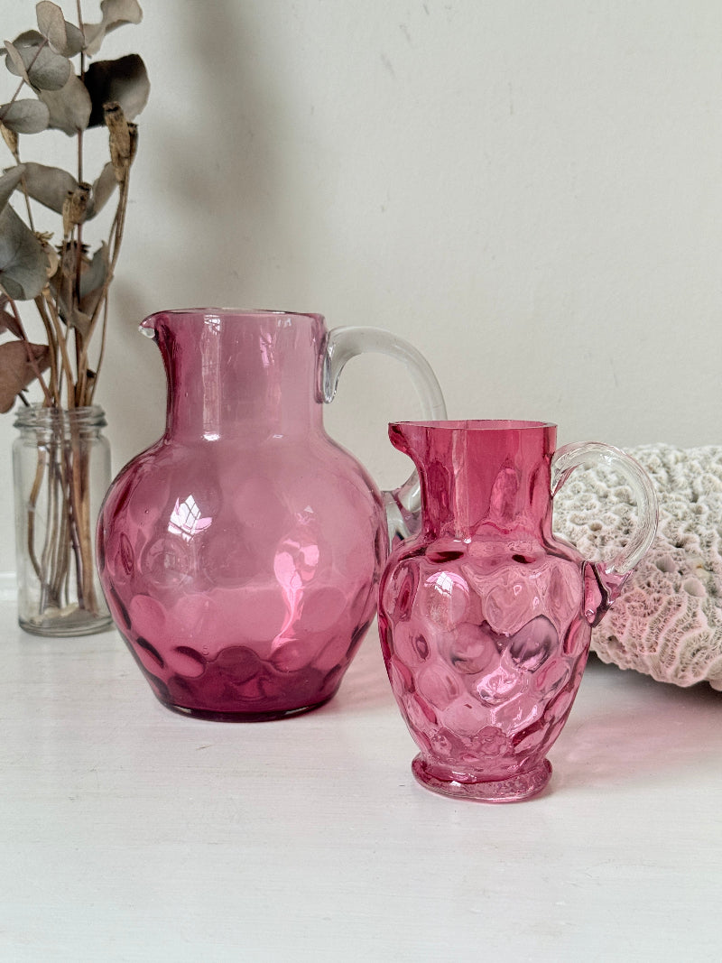 Vintage cranberry glass jugs, a pair with clear handles, photographed on a white surface