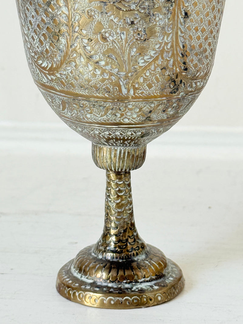 Indian Benares brass lidded vase with engraved figures and pedestal base, photographed on a white surface