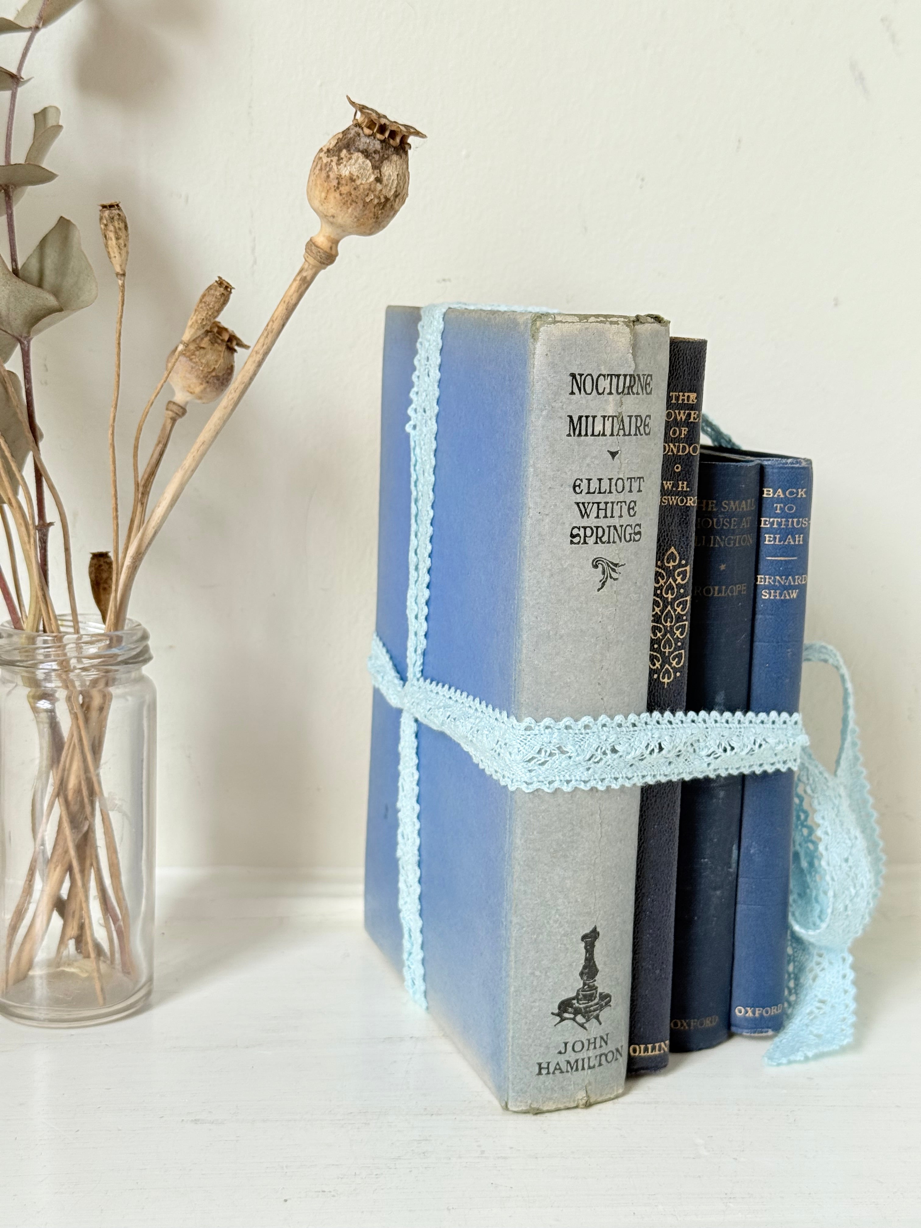 Vintage navy decorative book bundle tied with pale blue lace ribbon, photographed on a white surface