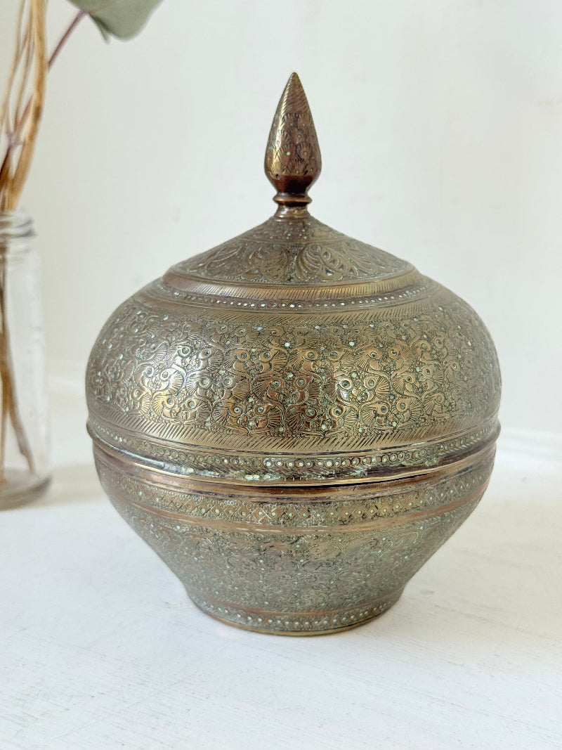 Indian Benares brass lidded jar with floral engraving and finial, photographed on a white surface