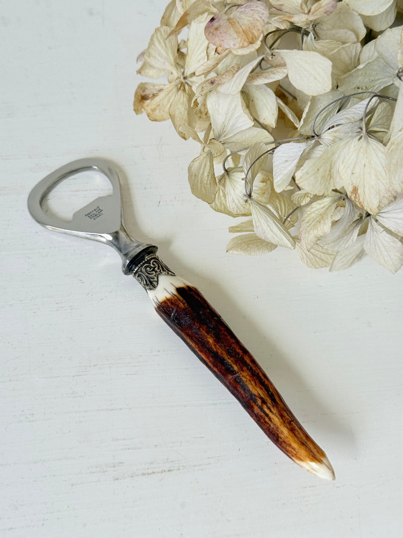 vintage antler handle bottle opener with stainless steel top photographed on white surface