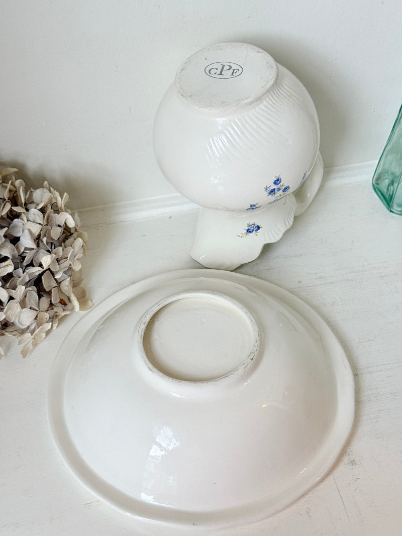 A white ceramic bowl with a blue floral pattern, shown upside down with its matching white lid placed in front of it on a white surface.