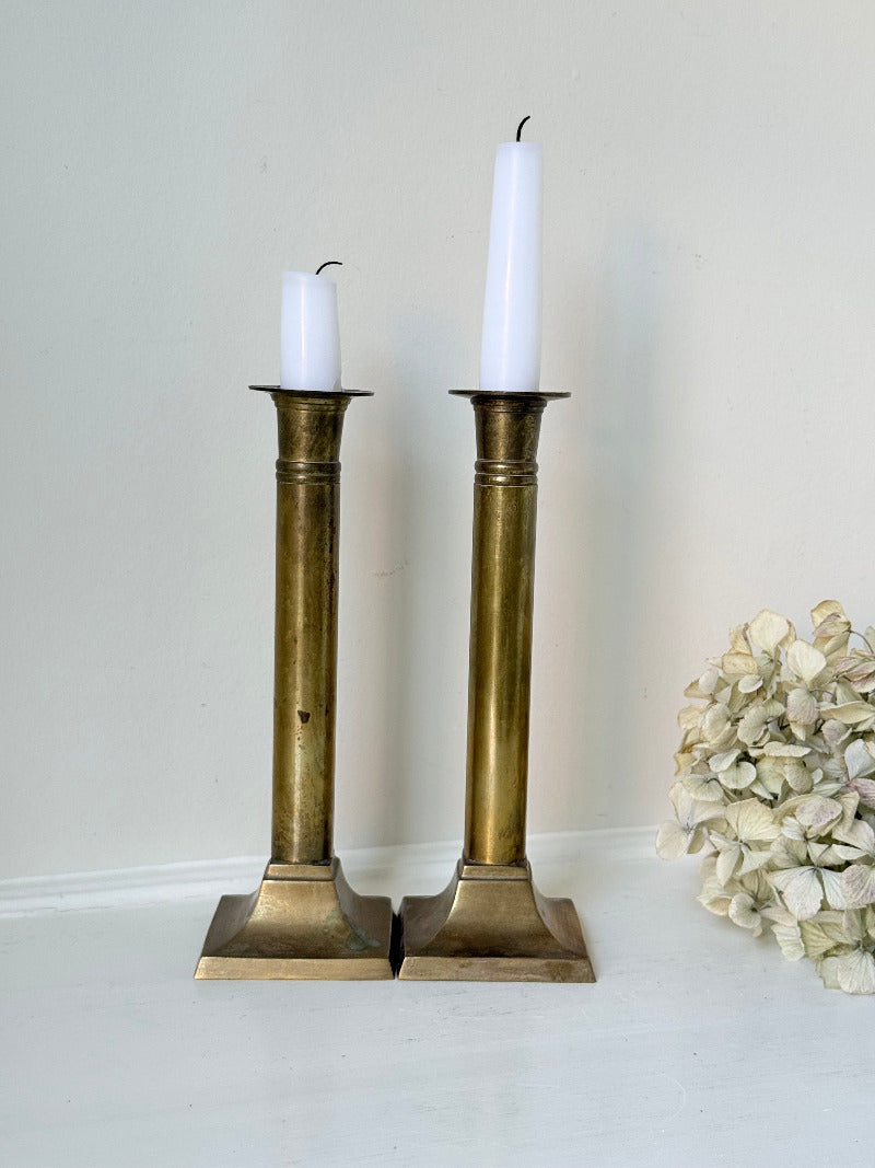 Pair of vintage brass candlesticks with square bases and white taper candles, styled on a white surface beside dried hydrangeas.