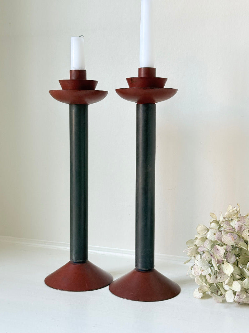 Pair of tall vintage metal candlesticks in black and burgundy, styled with white taper candles on a white surface.
