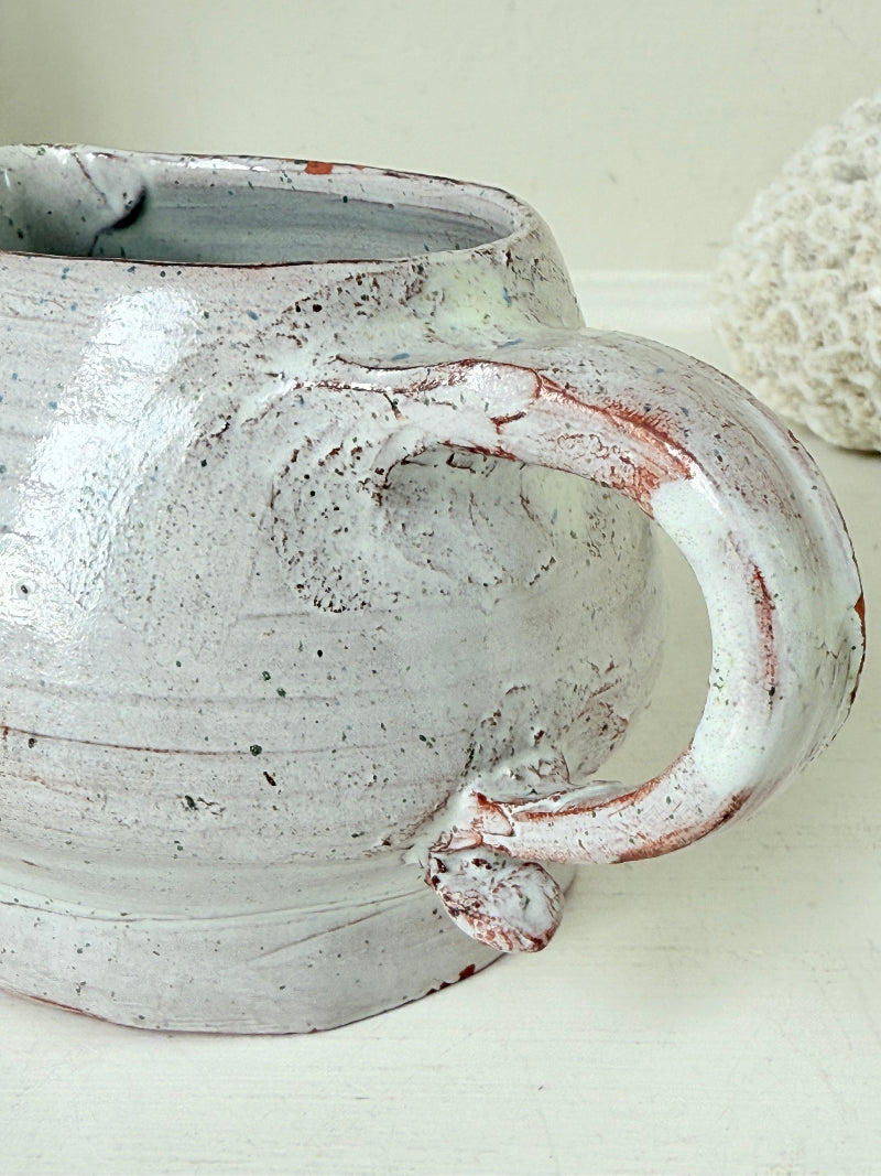 Studio pottery milk jug with soft pink and grey speckled glaze, photographed on a white surface