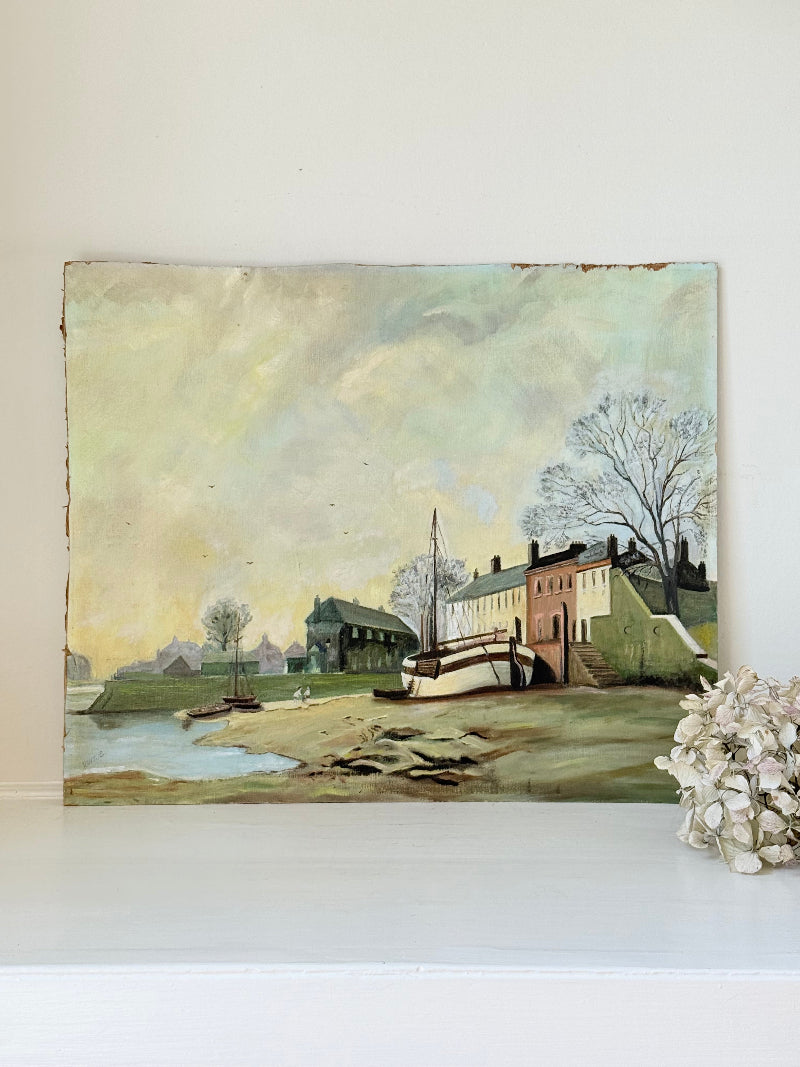 Vintage oil painting on board of a rural village scene with houses, trees, and water, photographed on a white surface