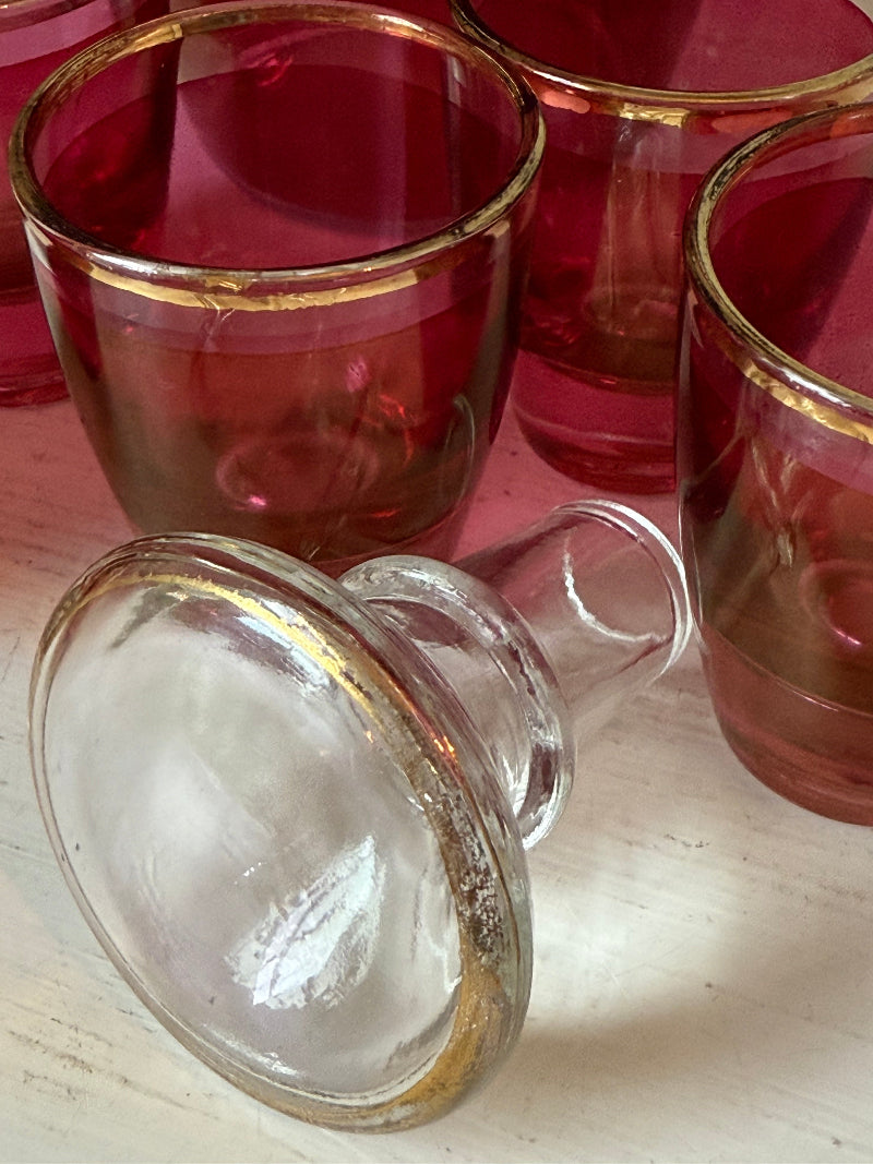 Vintage red printed glass cocktail set with clear glass decanter and six small glasses with gilt band rims, photographed on a white surface
