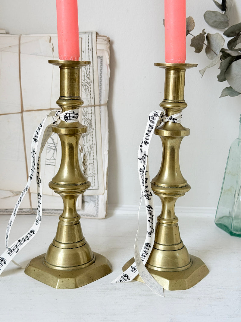 Pair of antique brass candlesticks with turned baluster stems and stepped bases holding coral tapers