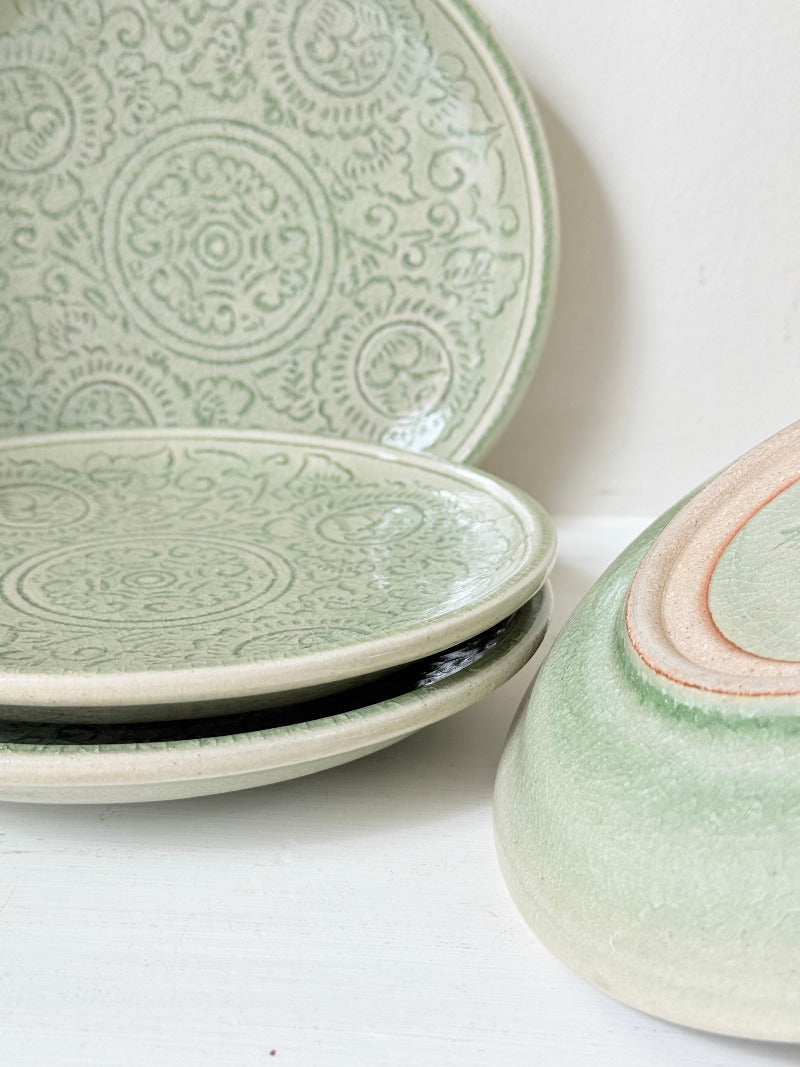 Set of four Thai celadon side plates with embossed patterns and sage green crackled glaze, stacked and photographed on white surface