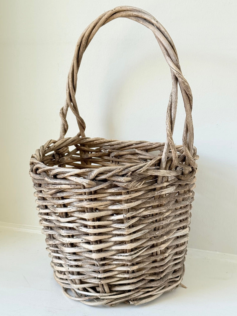 Rustic vintage wicker basket with woven handle and aged natural finish photographed on a white surface