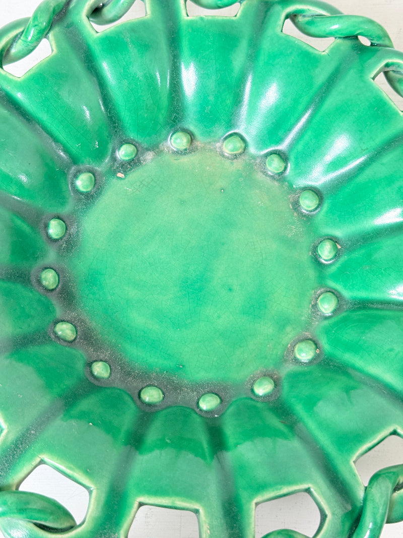 Close-up of a glossy green ceramic plate with a scalloped rim, raised circular details, and cutout sections near the edge.