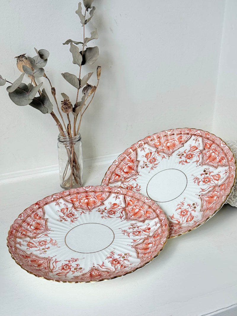 pair of vintage porcelain coral transfer plates with scalloped edges and gilt detail on white surface
