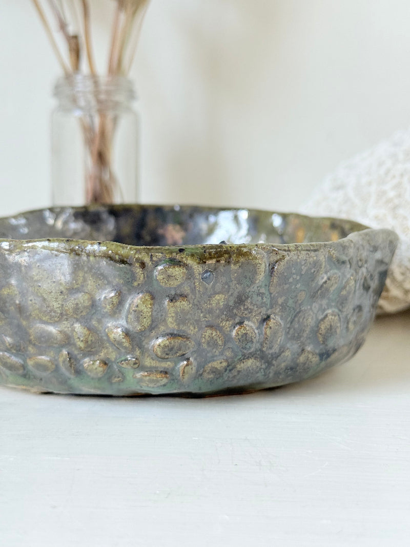 Studio pottery olive bowl with green and charcoal glaze, photographed on a white surface