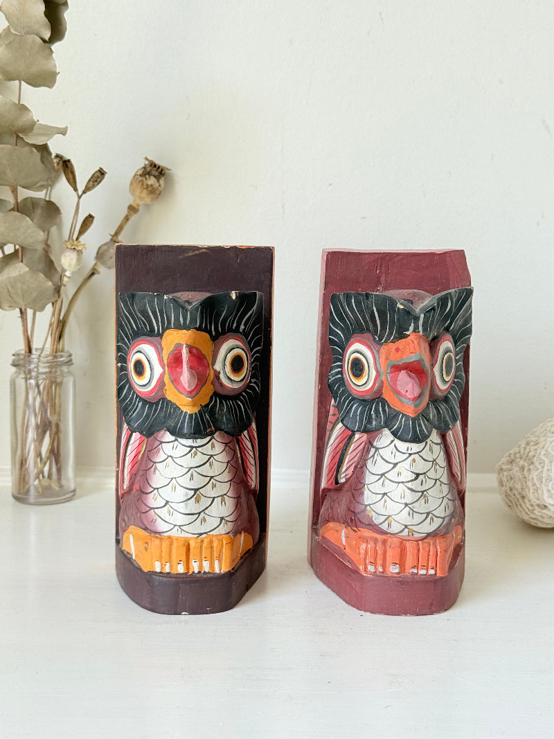 Vintage wooden owl bookends hand painted in red and orange tones, displayed on a white surface beside dried flowers.