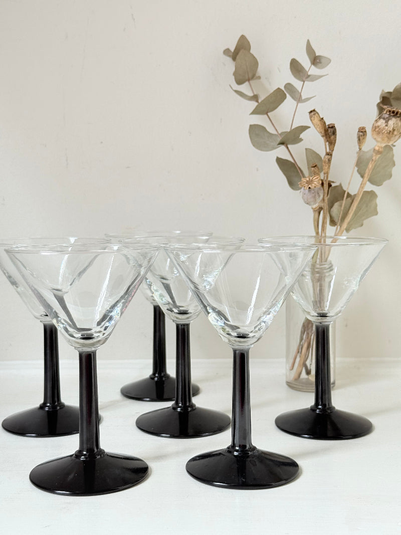 Set of six clear martini glasses with black stems, photographed on a white surface