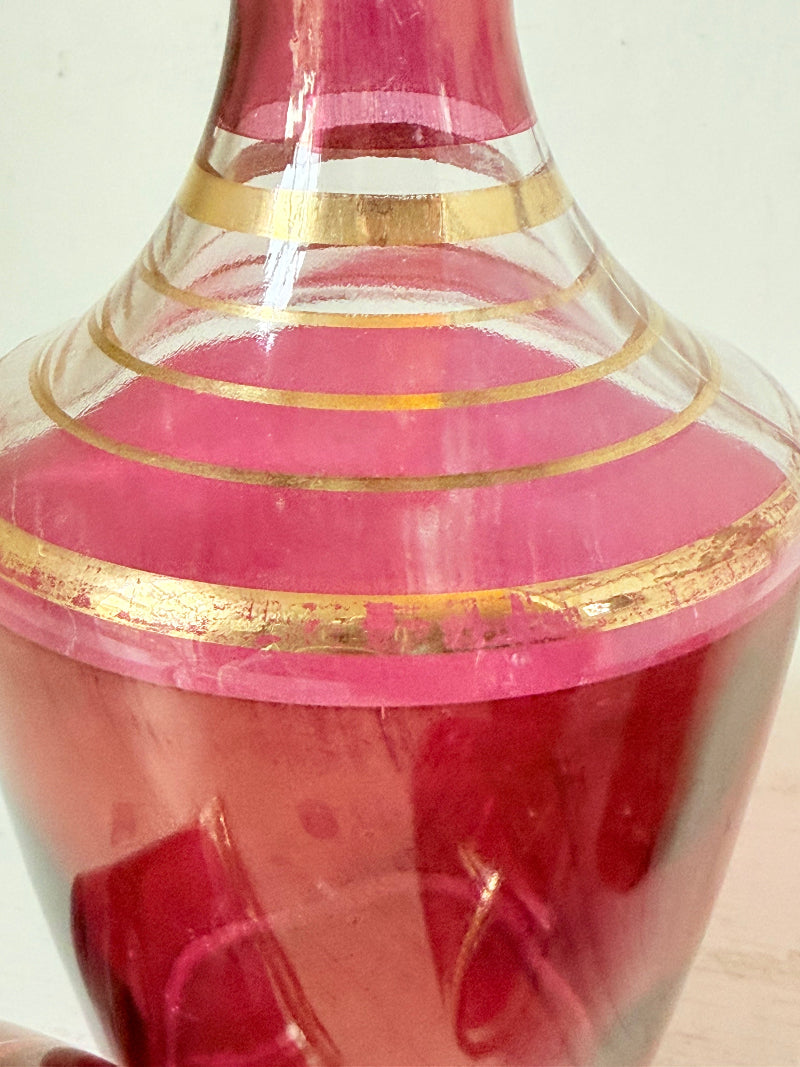 Vintage red printed glass cocktail set with clear glass decanter and six small glasses with gilt band rims, photographed on a white surface