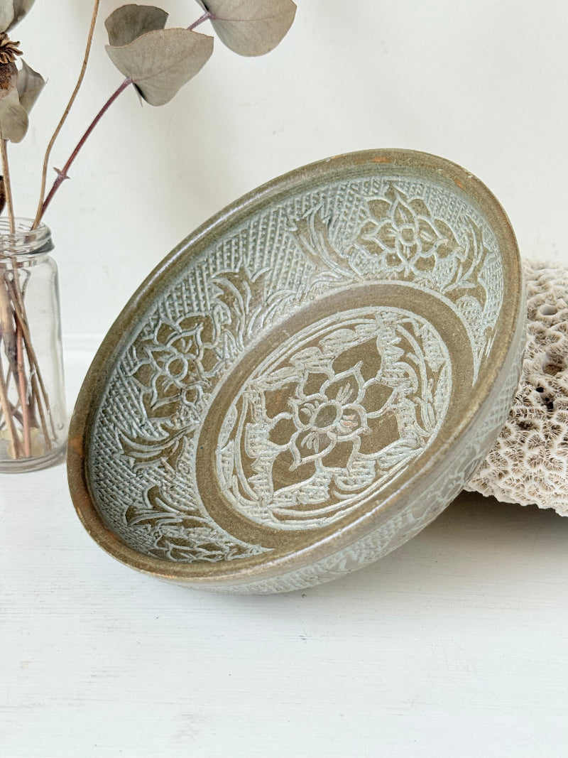 Studio pottery bowl with carved floral and geometric decoration in neutral glaze, photographed on a white surface with a pear inside.