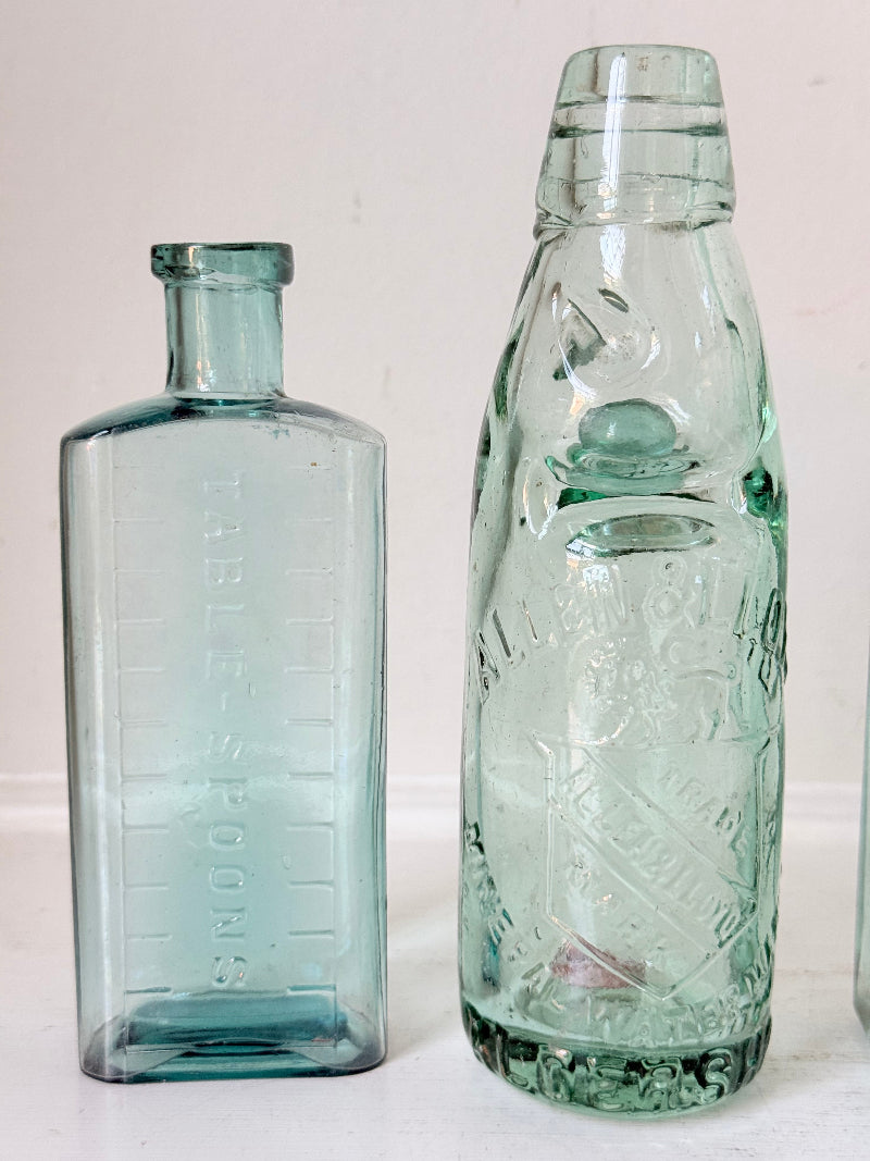 Set of five antique aqua green glass bottles with embossed lettering, photographed on a white surface