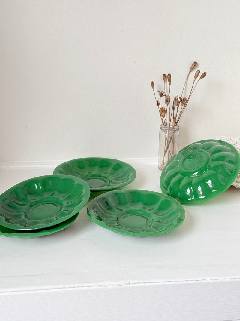 set of five vintage green pressed glass plates with decorative pattern, photographed on a white surface with dried flowers