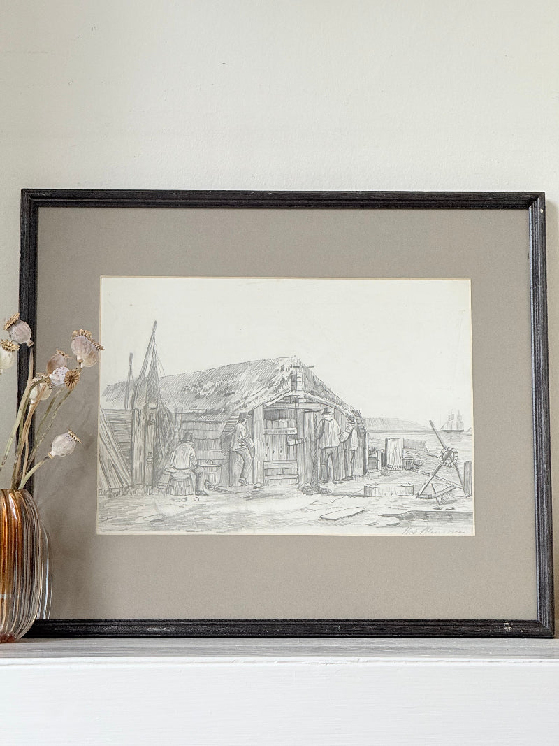 Vintage pencil drawing of rural scene with outbuildings and figures, under glass in black wooden frame, photographed on white surface.