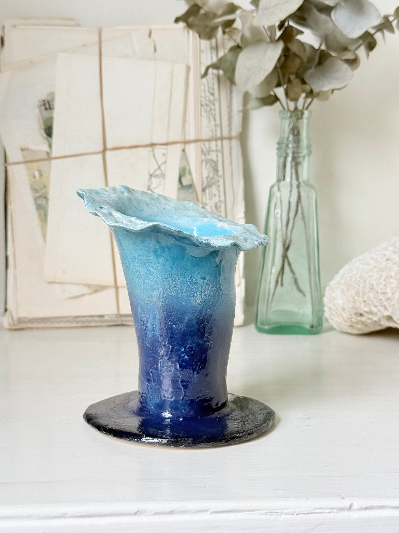 Handmade studio pottery trumpet vase in ombre blue with a frilled rim, photographed on a white surface