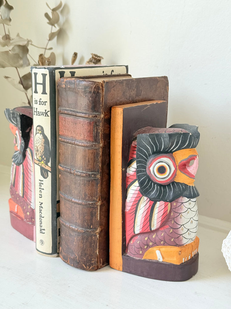 Vintage wooden owl bookends hand painted in red and orange tones, displayed on a white surface beside dried flowers.