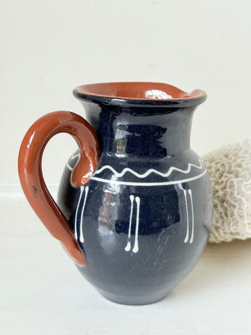 Slipware studio pottery jug with blue glaze and terracotta handle, photographed on a white surface