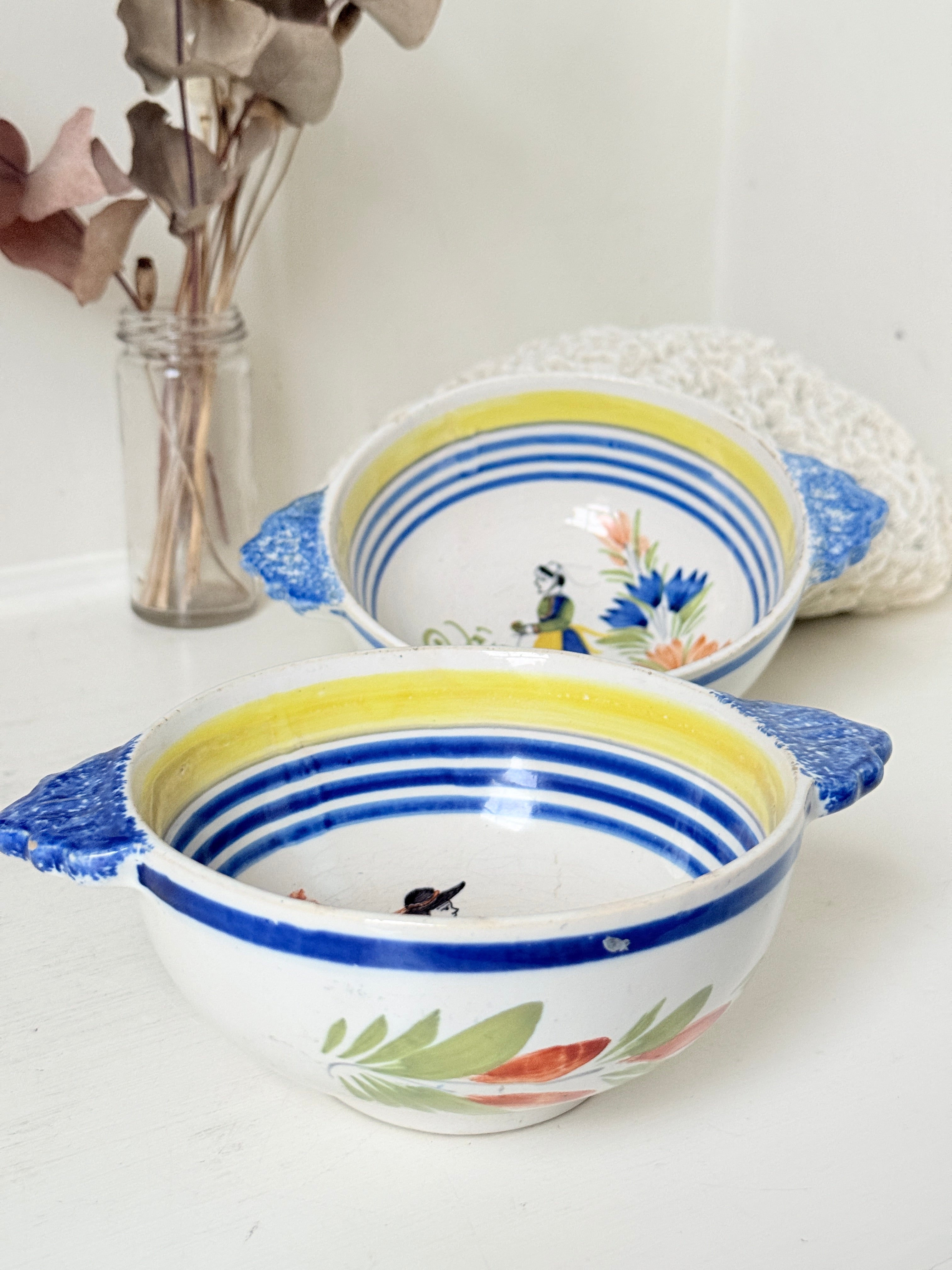 Pair of vintage French Quimper Breton figure bowls with blue handles, photographed on a white surface