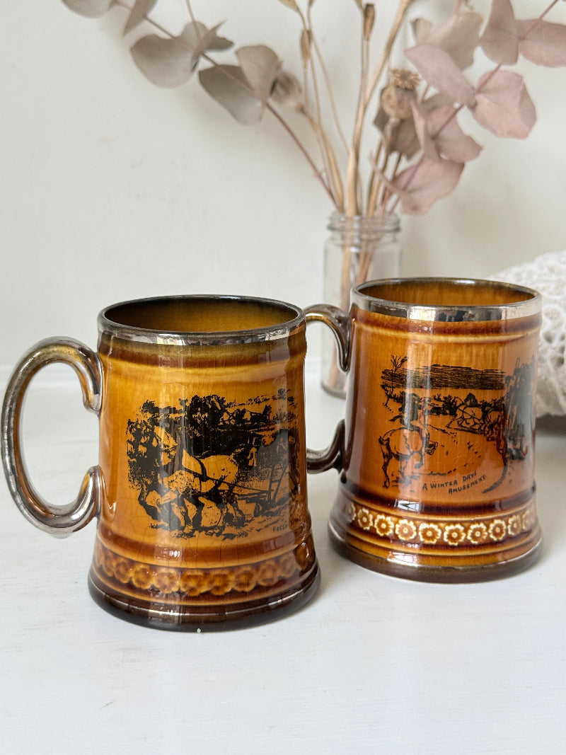 Pair of Ridgways stoneware tankard mugs photographed on a white surface in amber brown glaze with black Coaching Days and Coaching Ways transfer scenes