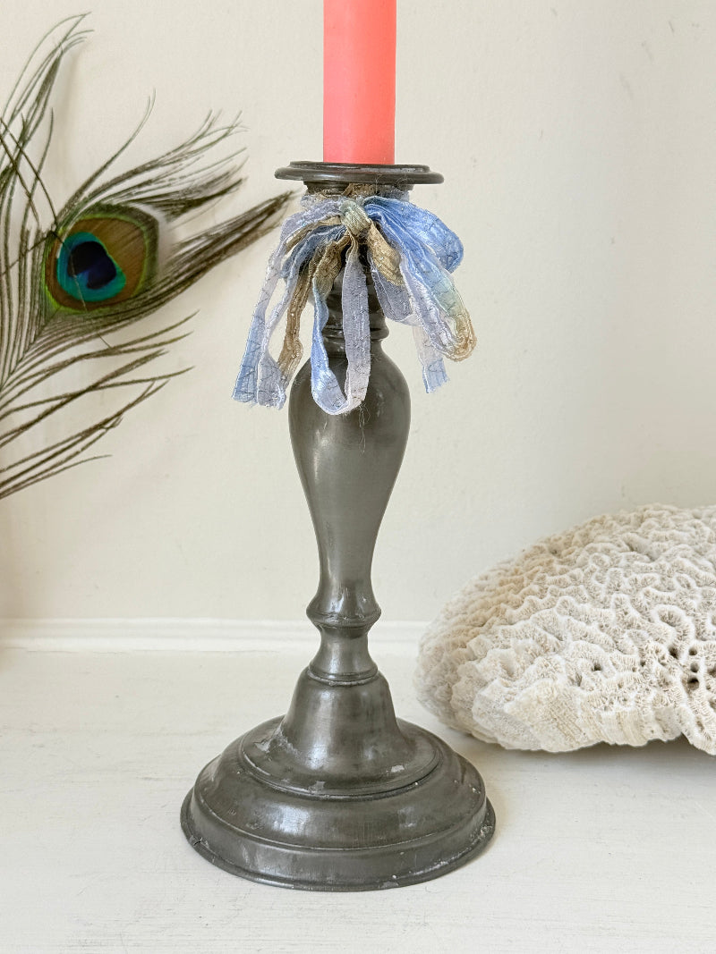 Antique pewter candlestick with baluster stem and aged patina styled with coral candle on white surface