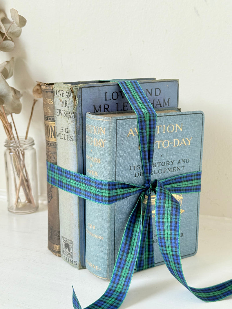Vintage blue fabric bound decorative book bundle tied with blue and green tartan ribbon, photographed on a white surface