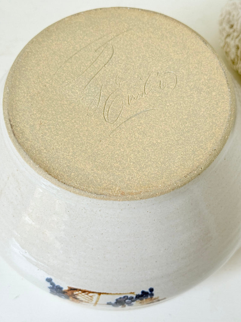 Large studio pottery bowl with hand-painted grape motif and side handles, photographed on a white surface