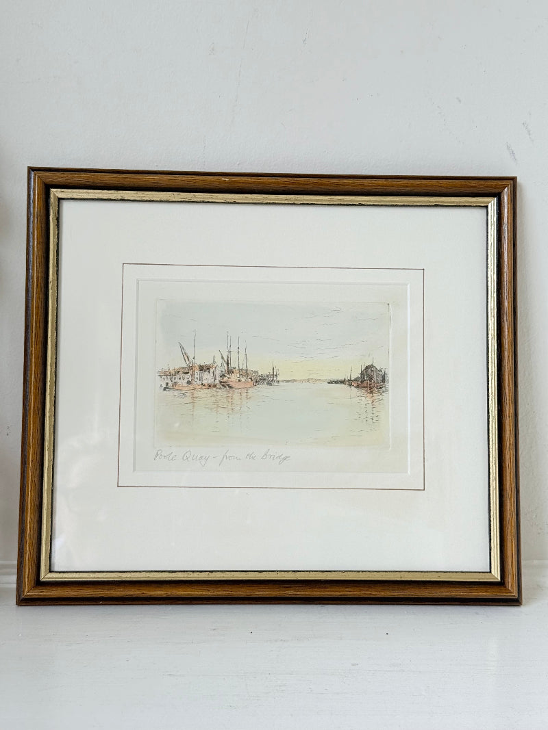 Framed vintage print of Poole Quay harbour scene in muted tones, under glass with gilt and wood-effect frame, on white surface.
