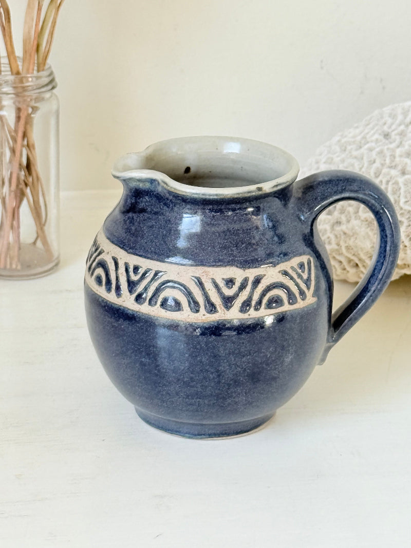 Studio pottery milk jug with deep blue glaze and cream geometric band, photographed on a white surface