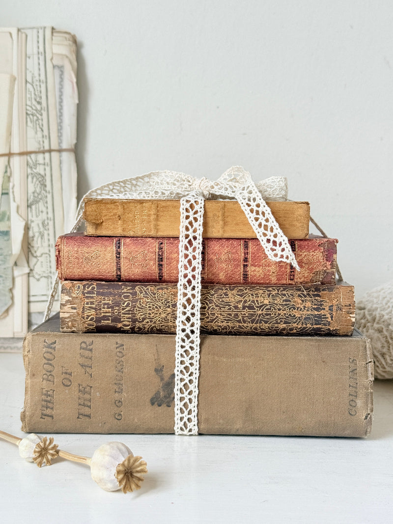Antique decorative book bundle with faded hardback covers, aged pages and neutral lace tie for vintage interior styling